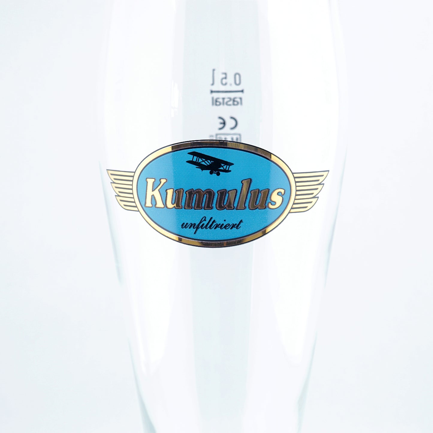 Nahaufnahme eines 0,5-Liter-Weißbierglases mit blau-goldenem Kumulus-Logo und der Aufschrift „unfiltriert“, auf weißem Hintergrund.
