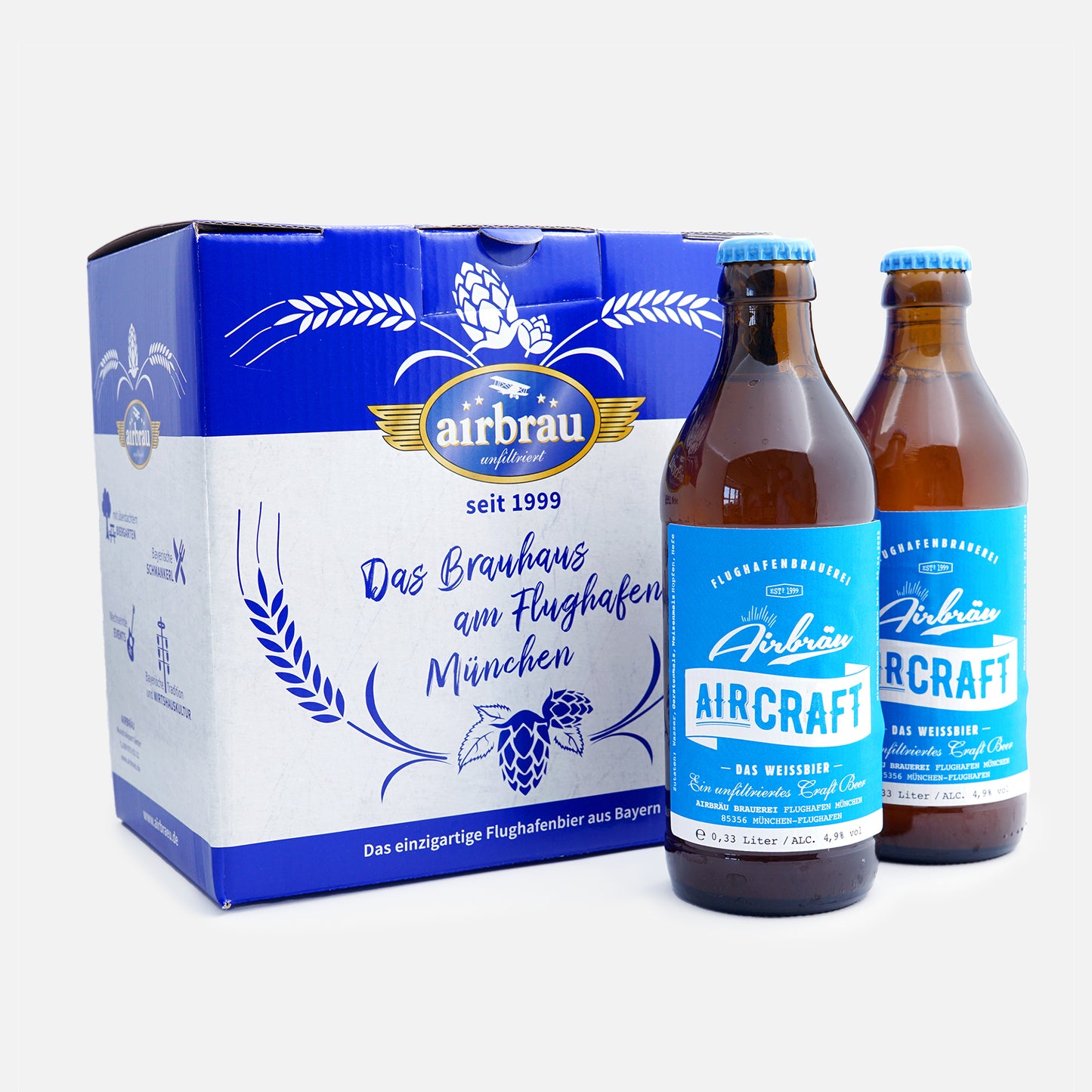 Zwei Flaschen Airbräu Aircraft Das Weissbier mit blauem Etikett vor einer blau-weißen Bierkartonverpackung mit dem Aufdruck „Das Brauhaus am Flughafen München".