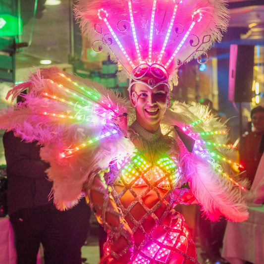 Strahlende Tänzerin in farbenfrohem LED-Kostüm mit Federn und Lichtern bei einer Showeinlage.