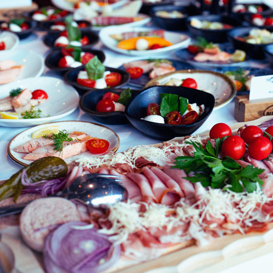 Buffet mit Aufschnitt, Käse, Tomaten, Gurken und weiteren kalten Vorspeisen auf Tellern angerichtet.