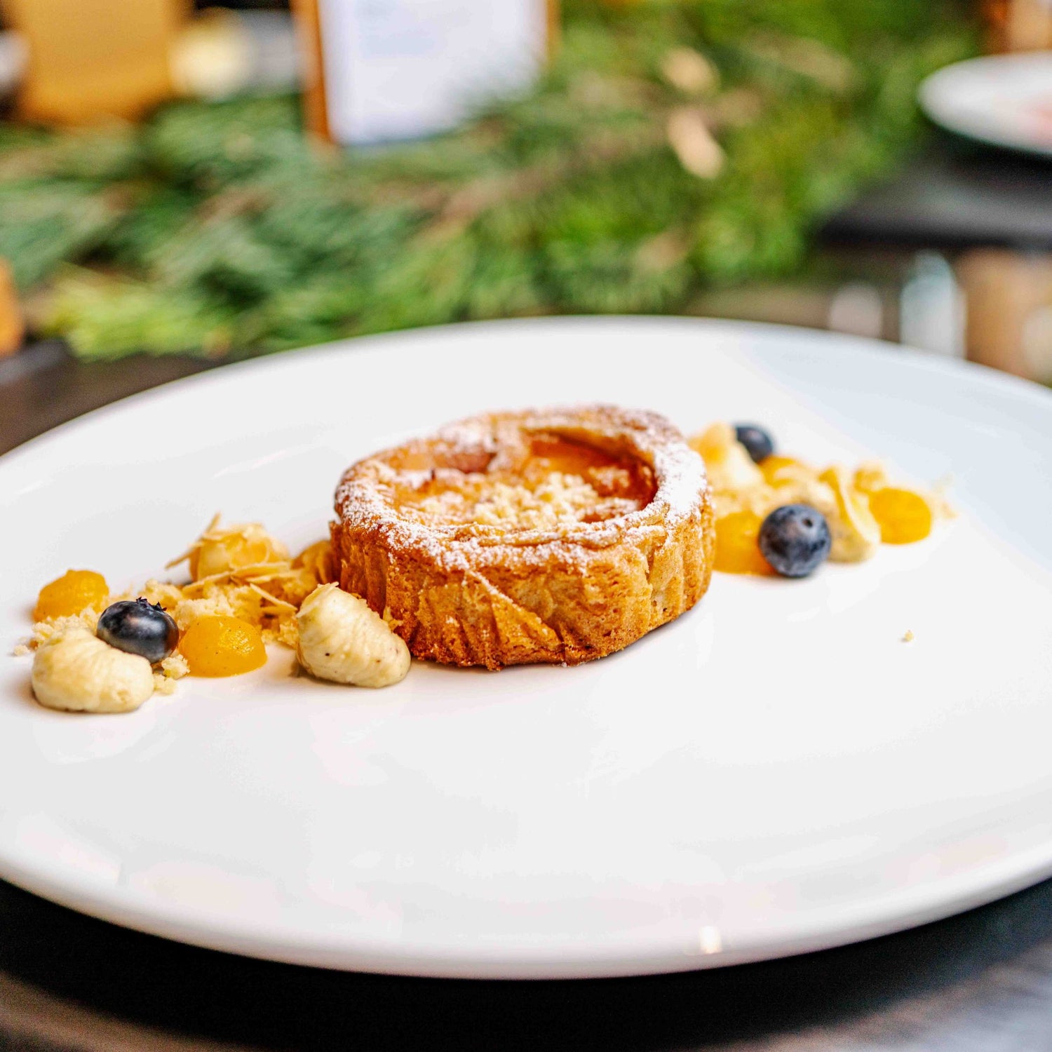 Feiner Vanillekipferl-Cheesecake mit Mandarinengelee, serviert mit frischen Blaubeeren und knusprigen Keksstückchen auf einem weißen Teller.