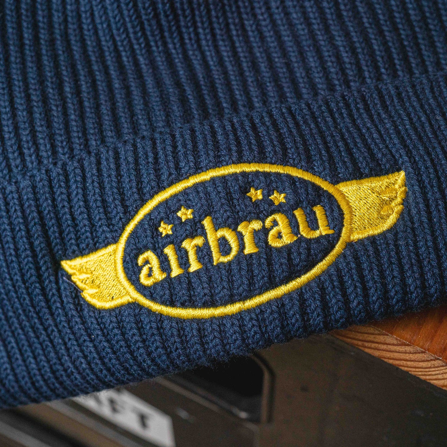 Dunkelblaue Strickmütze mit gesticktem, gelbem Airbräu-Logo und Flügel-Design.