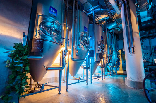 Innenansicht der Airbräu-Brauerei mit mehreren großen, beleuchteten Edelstahltanks zur Bierherstellung, umgeben von Rohren und industriellen Anlagen.